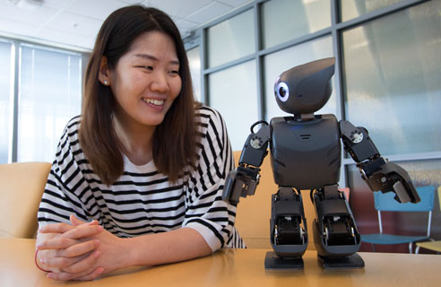 A student smiling at the robot she is working with