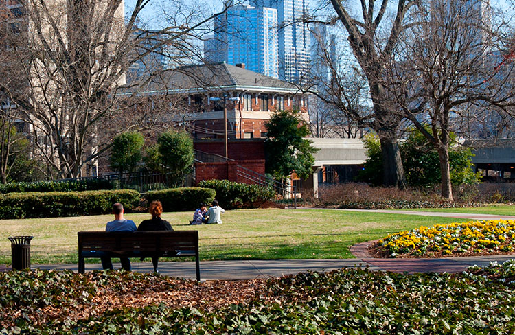 A view of campus in the summer with people relaxing on a memorial bench