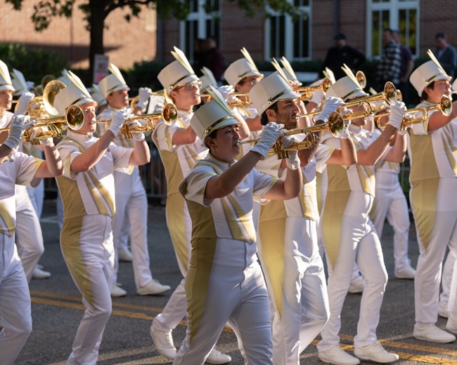 marching band trumpet section marching in white and gold uniforms while playing